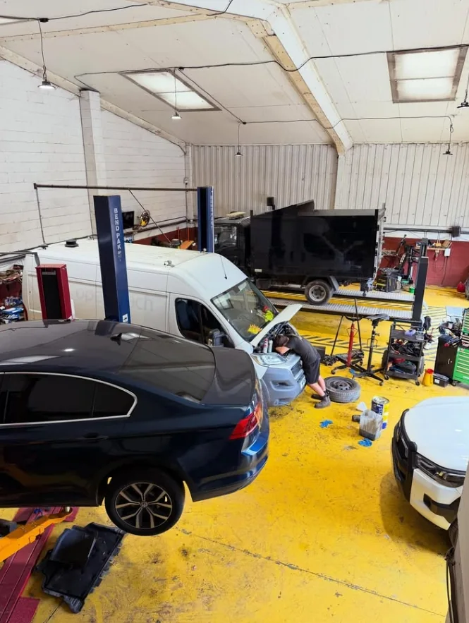 Technician working under a van bonnet in a busy workshop